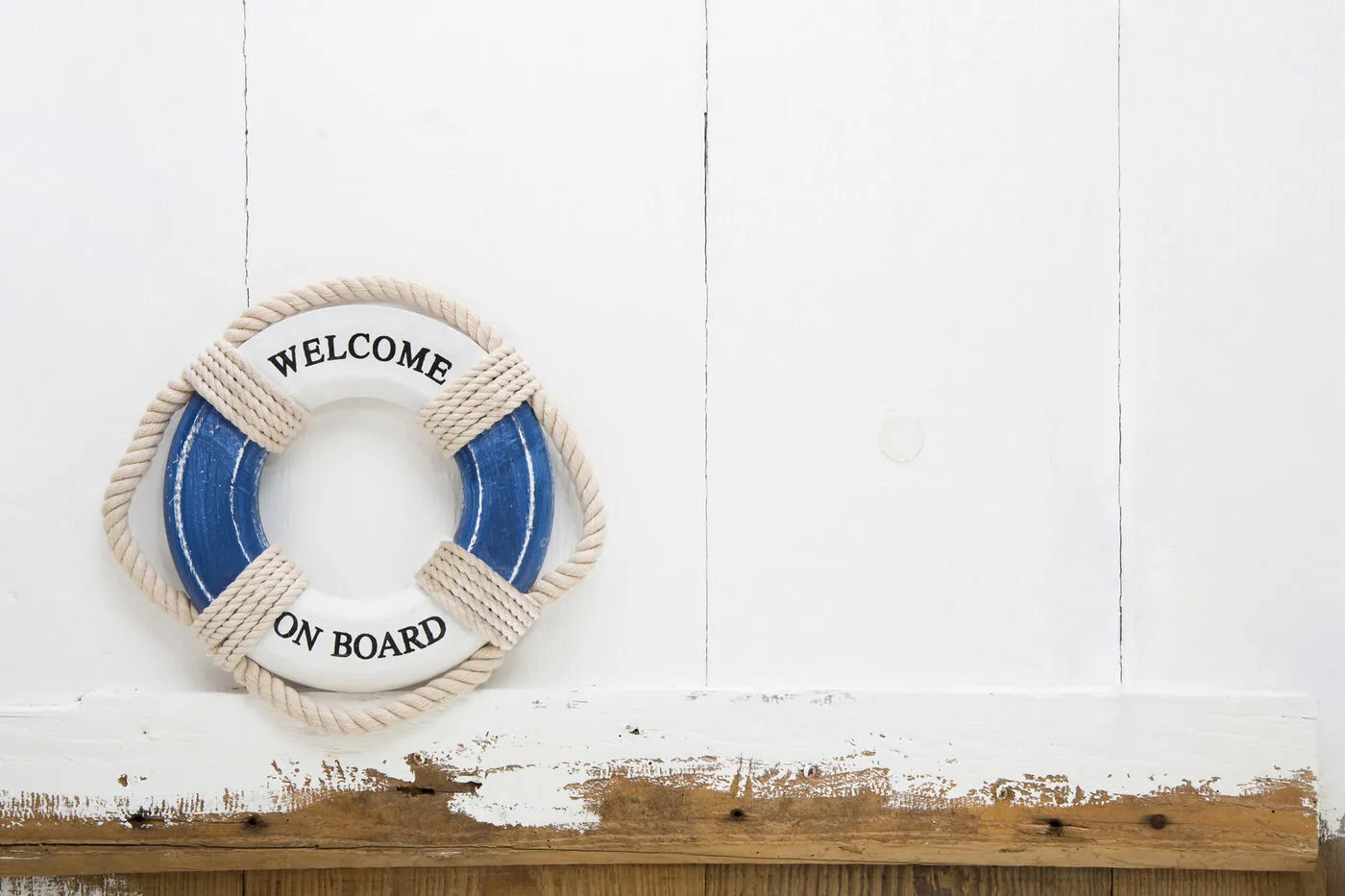 Ein blau-weißer Rettungsring mit der Aufschrift „Welcome on board“ an einer weißen Holzwand.